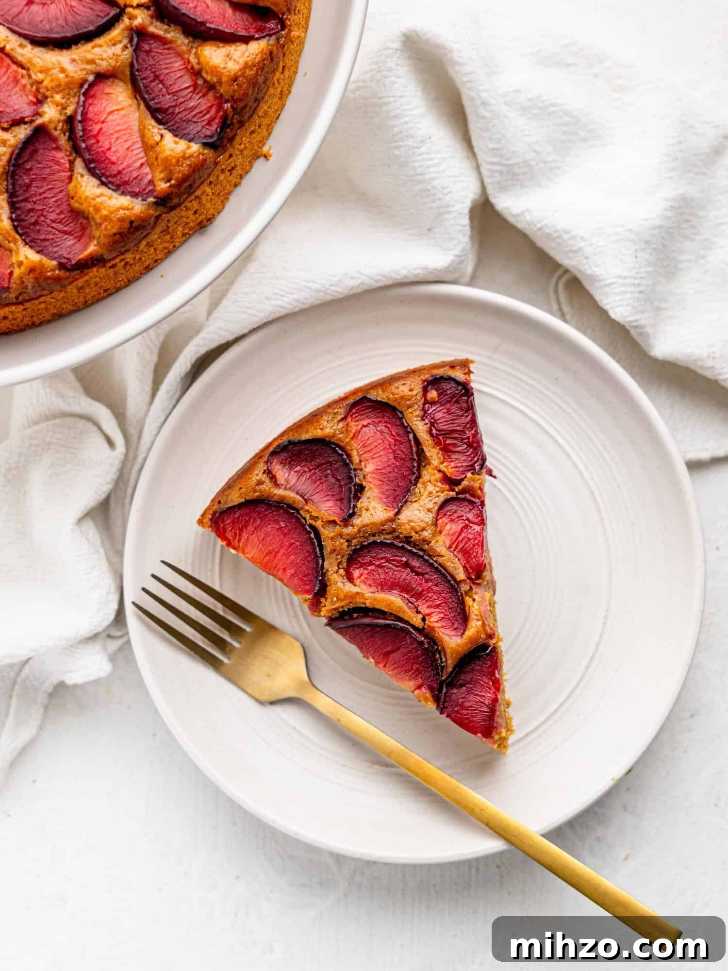 A slice of yogurt plum cake on a white plate - bird's eye view.