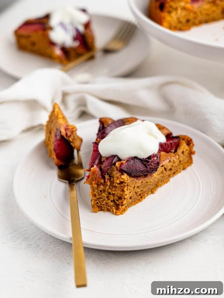A slice of yogurt plum cake served with yogurt on a white plate.