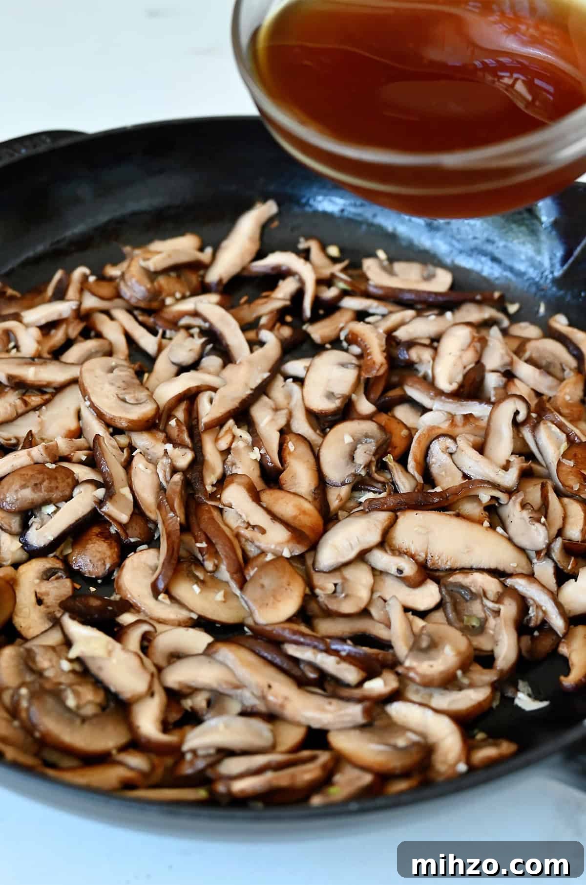 Creamy Garlic Mushroom Sauce for Pasta and Steak 7 Adding beef stock to a large skillet with sautéed mushrooms and garlic.