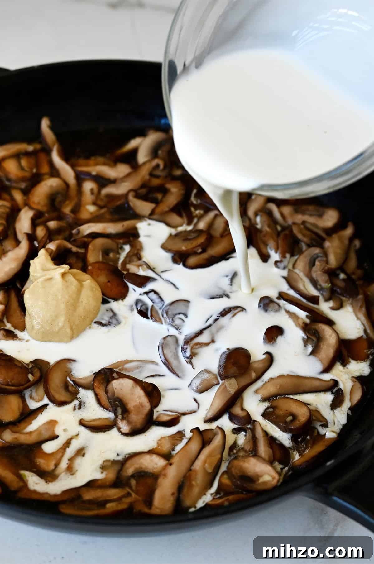 Creamy Garlic Mushroom Sauce for Pasta and Steak 8 Adding heavy cream from a liquid measuring cup to a pan with sautéed mushrooms, garlic, beef broth and Dijon mustard to make a mushroom cream sauce.