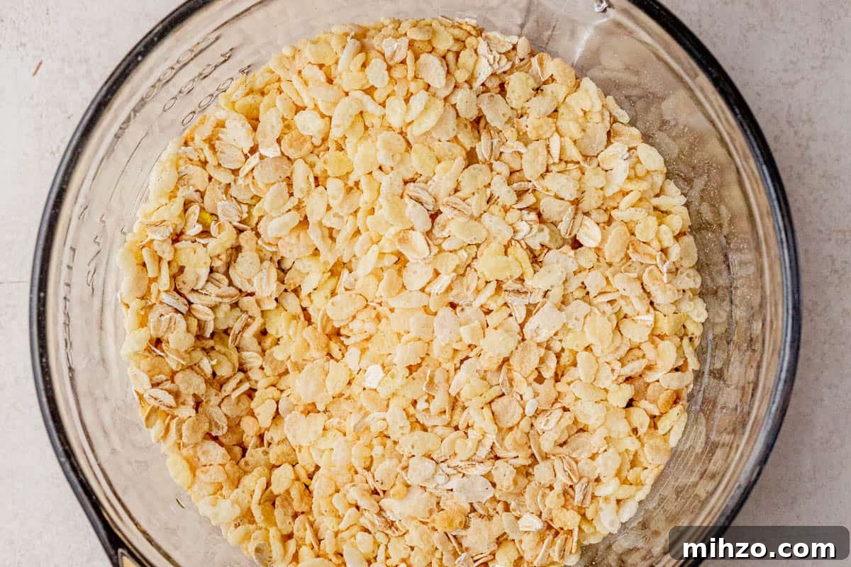 Close-up of a glass mixing bowl filled with a combination of rolled oats and puffed rice cereal on a neutral kitchen counter.