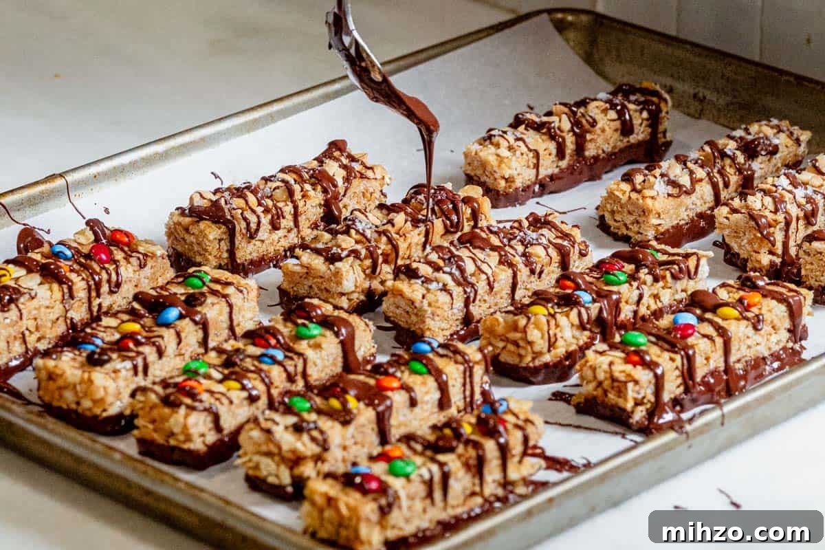 Tray of no-bake copycat Kudos bars with rice cereal, oats, and peanut butter being drizzled with melted chocolate.