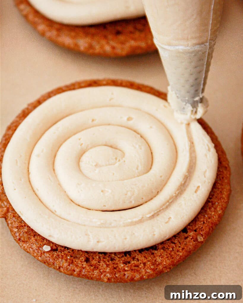 Gingerbread Sandwich Cookies Recipe for the Holidays 9 Piping cream filling on gingerbread cookie. Beige background.