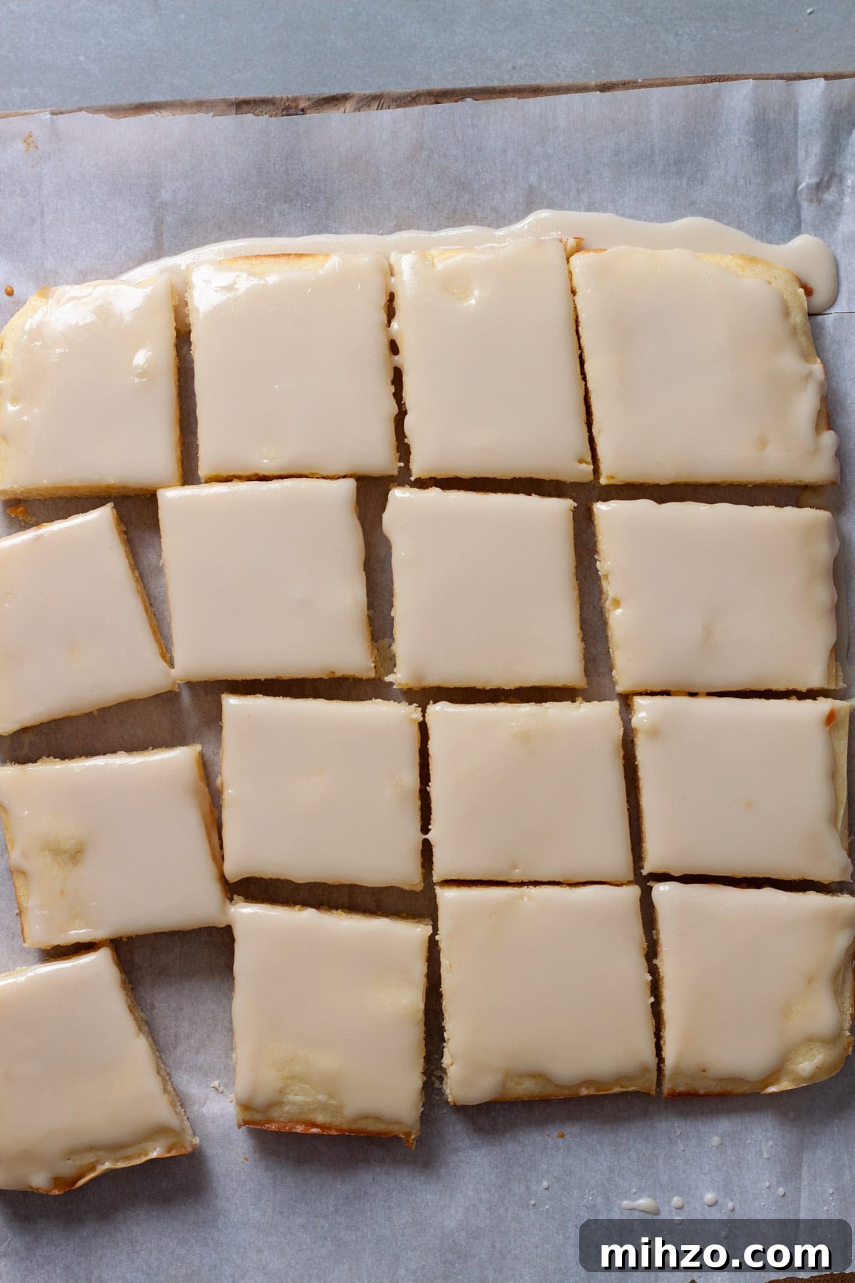Zesty Lemon Blondies with Luscious Glaze 12 Lemon blondies topped with lemon icing cut up on a piece of parchment paper on a cutting board.