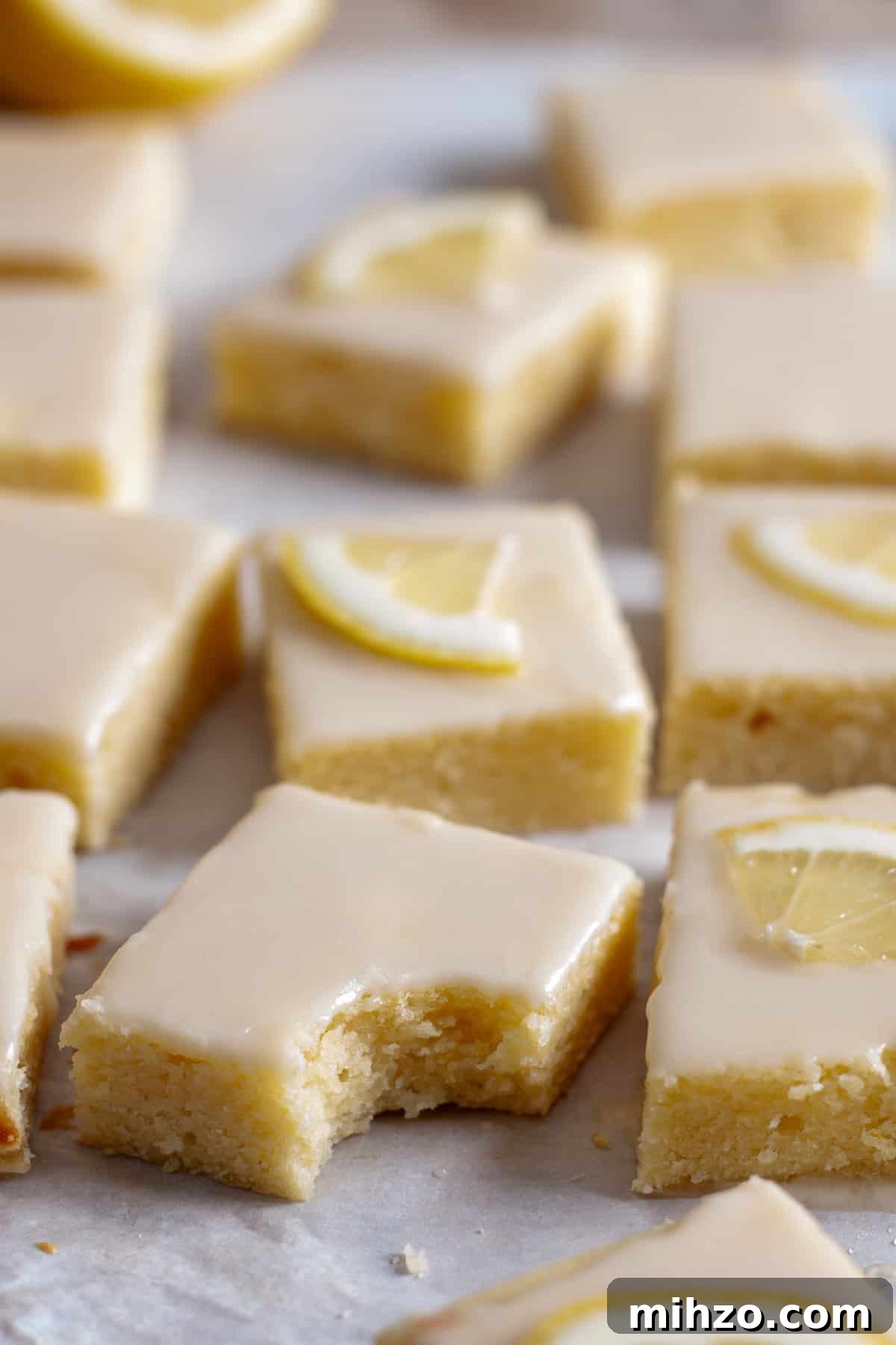 Zesty Lemon Blondies with Luscious Glaze 14 Lemon blondies on parchment paper and one blondie has a bite taken out of it.