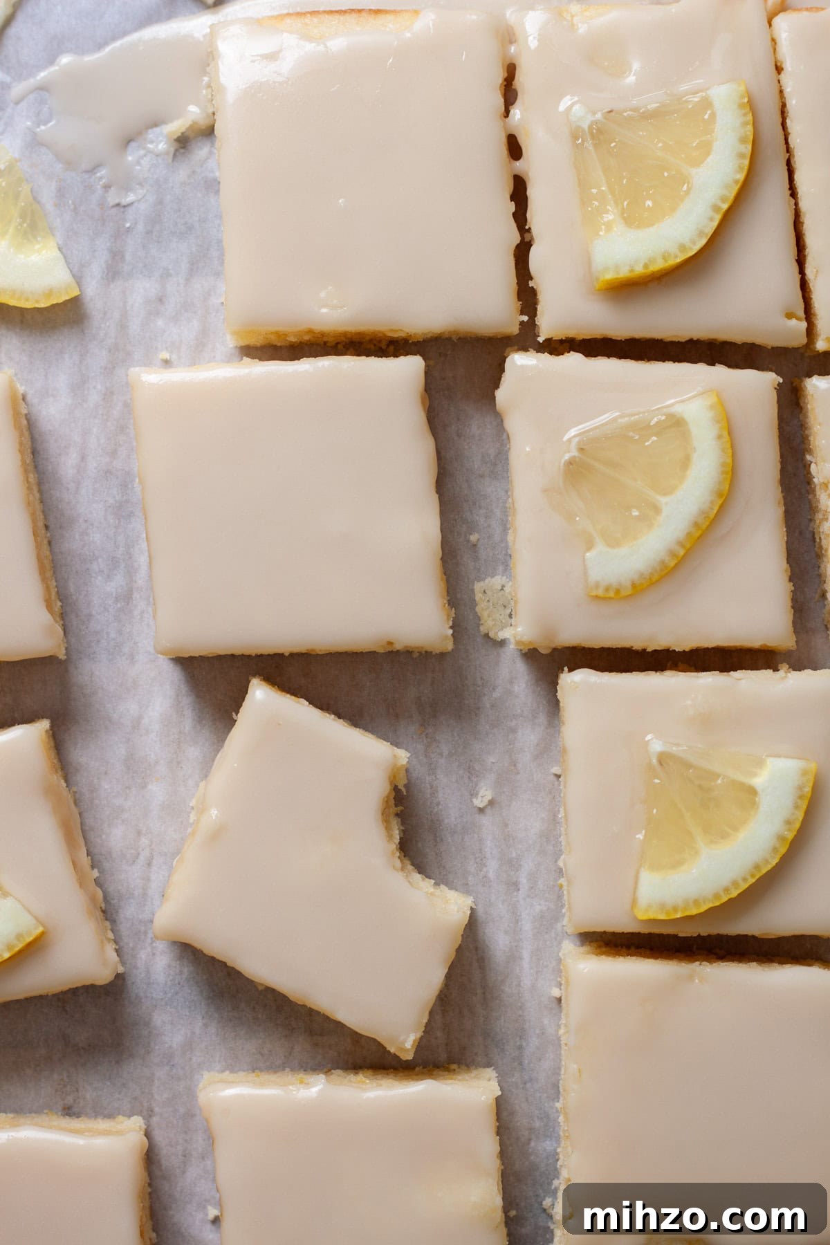 Zesty Lemon Blondies with Luscious Glaze 16 Lemon blondies topped with thin slices of lemon on a piece of parchment paper.