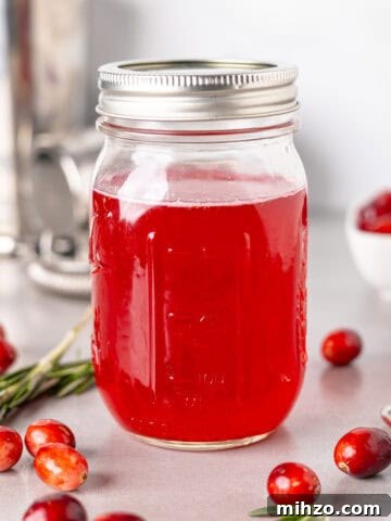 Zesty Lemon Blondies with Luscious Glaze 18 A mason jar with bright red cranberry simple syrup and fresh cranberries spread around the table.
