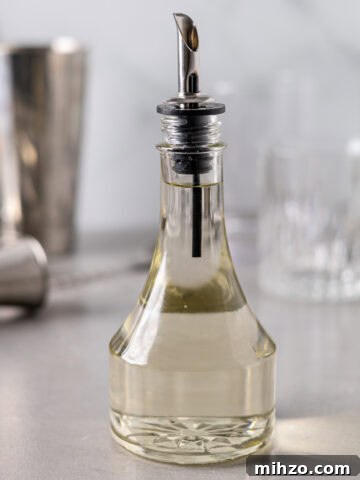 Zesty Lemon Blondies with Luscious Glaze 19 A glass bottle with a sprout on top filled with a clear simple syrup liquid and cocktail mixing tools in the background.