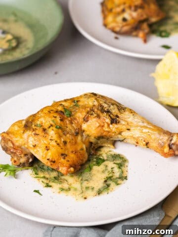 Zesty Lemon Blondies with Luscious Glaze 21 A serving of golden brown roasted chicken leg quarters with an herb sauce on a gray table with more chicken in the background.