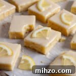 Lemon blondies topped with thin slices of lemon on a piece of parchment paper.