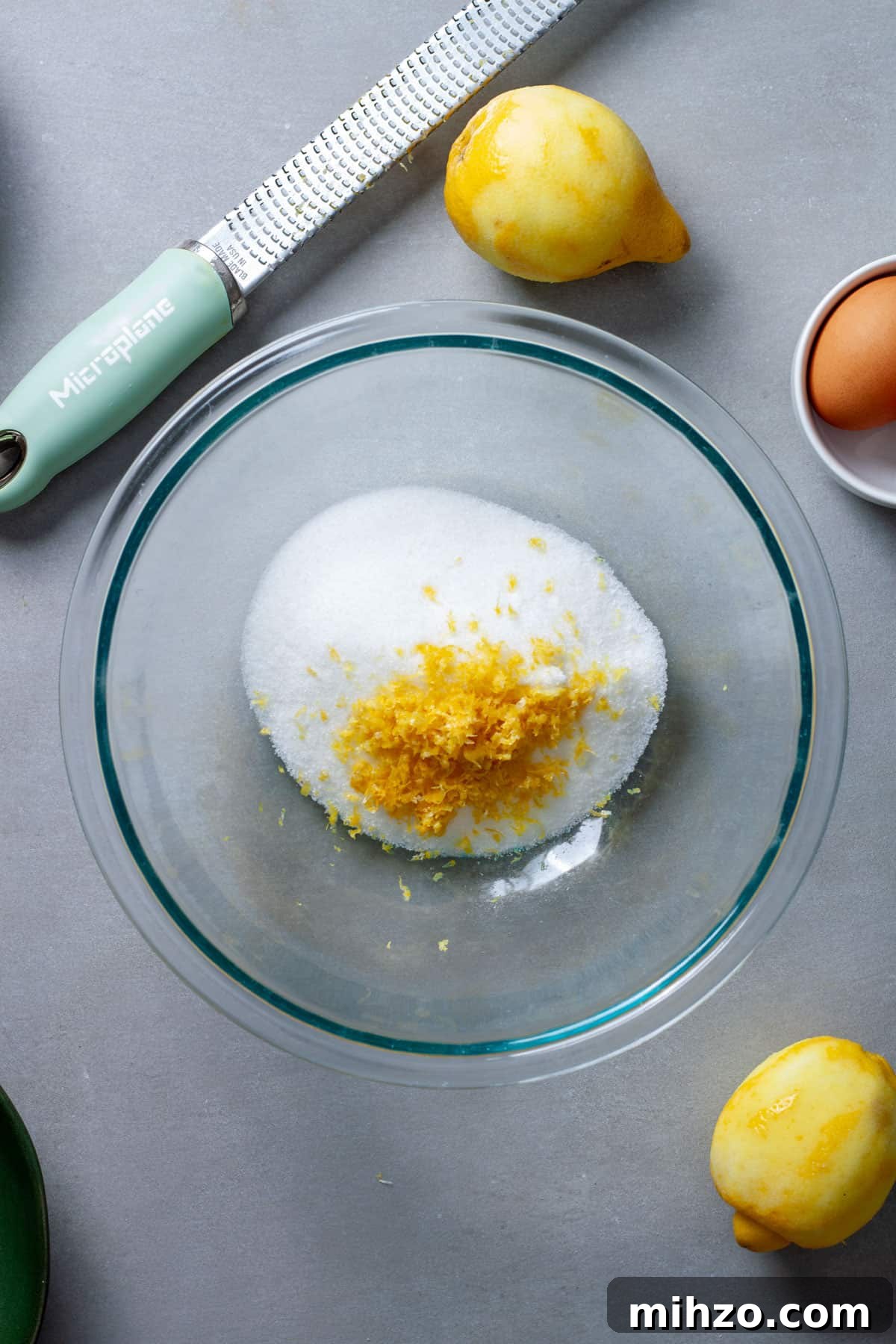 Zesty Lemon Blondies with Luscious Glaze 4 Lemon zest grated into sugar in a glass bowl on a gray table.