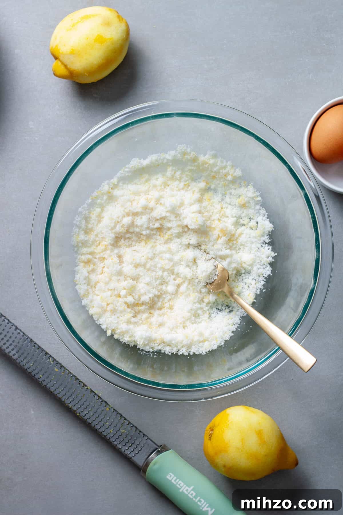 Zesty Lemon Blondies with Luscious Glaze 5 A fork mashing lemon zest into granulated sugar in a glass bowl on a gray table.