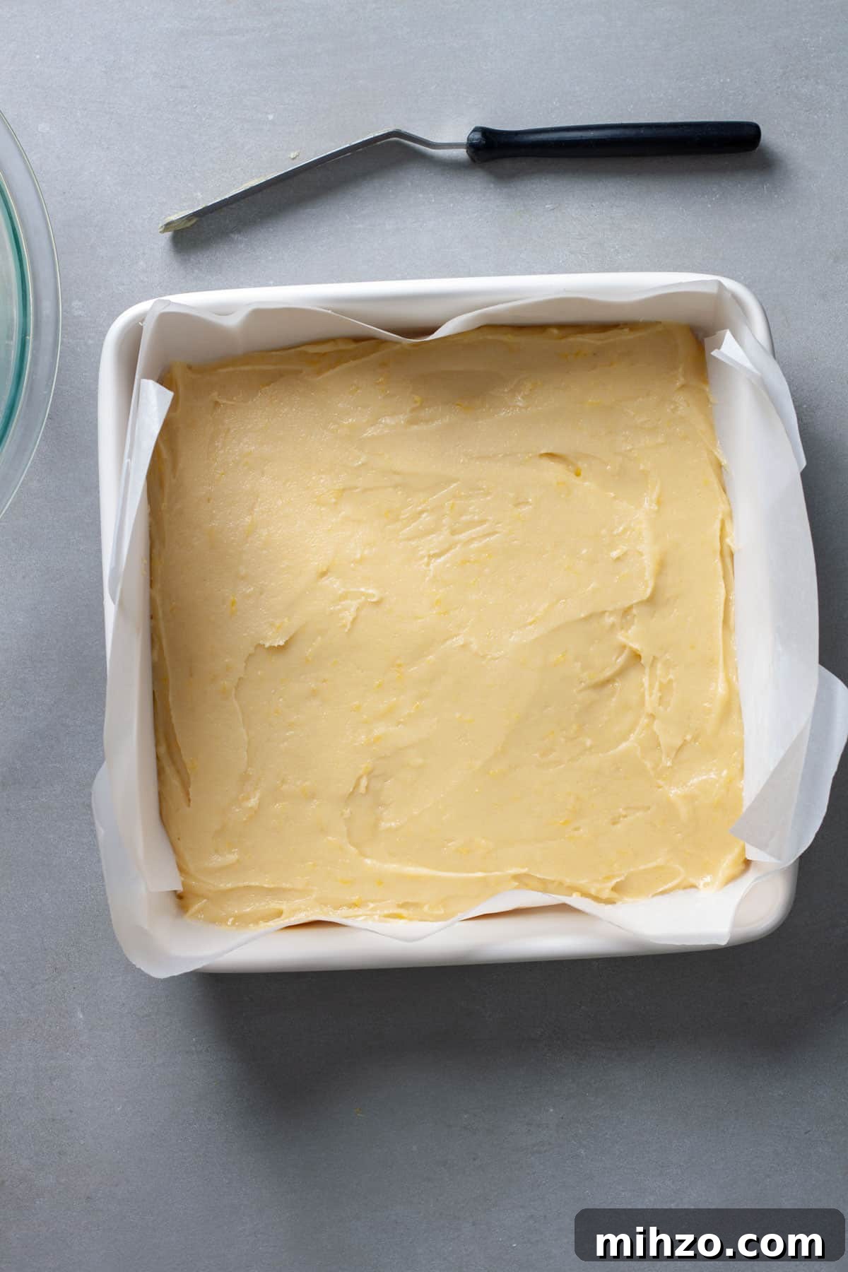 Zesty Lemon Blondies with Luscious Glaze 8 Lemon blondies unbaked in a parchment lined square baking dish on a gray table.