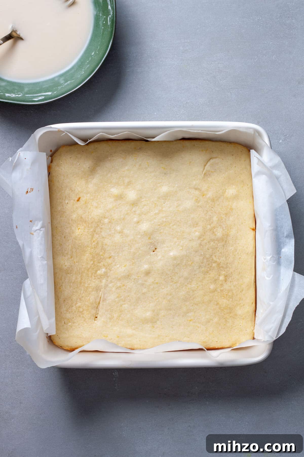 Zesty Lemon Blondies with Luscious Glaze 10 Lemon blondies fresh out of the oven cooling on a gray table with icing off to the side.