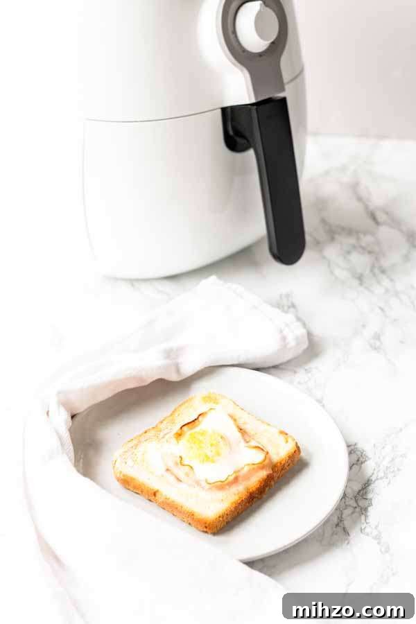 Crispy Bacon and Egg Toast Made in the Air Fryer 8 Egg toast with bacon on a white plate with Air Fryer in the back