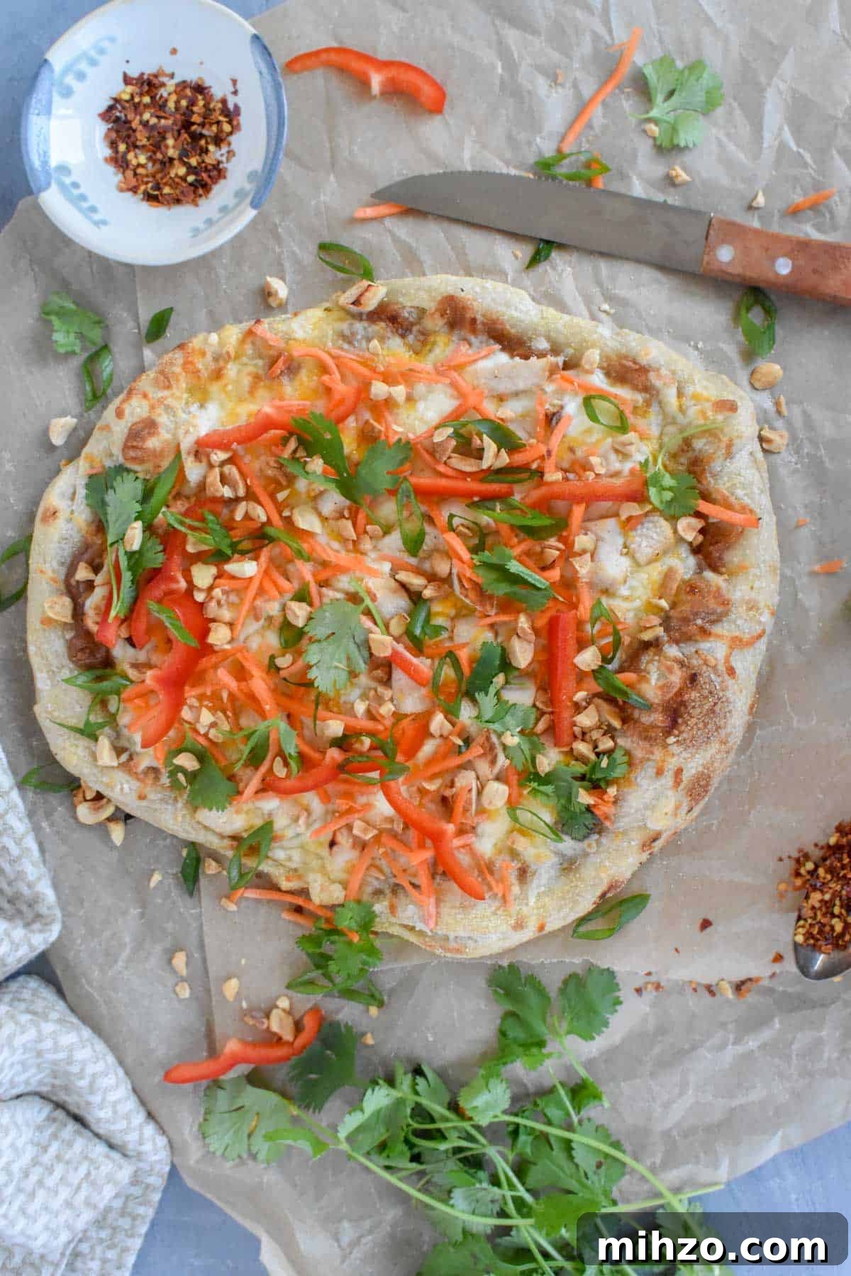 Thai Chicken Pizza Recipe: Tangy Peanut Sauce & Crispy Crust 2 whole pizza on brown parchment paper with fresh herbs scattered around.