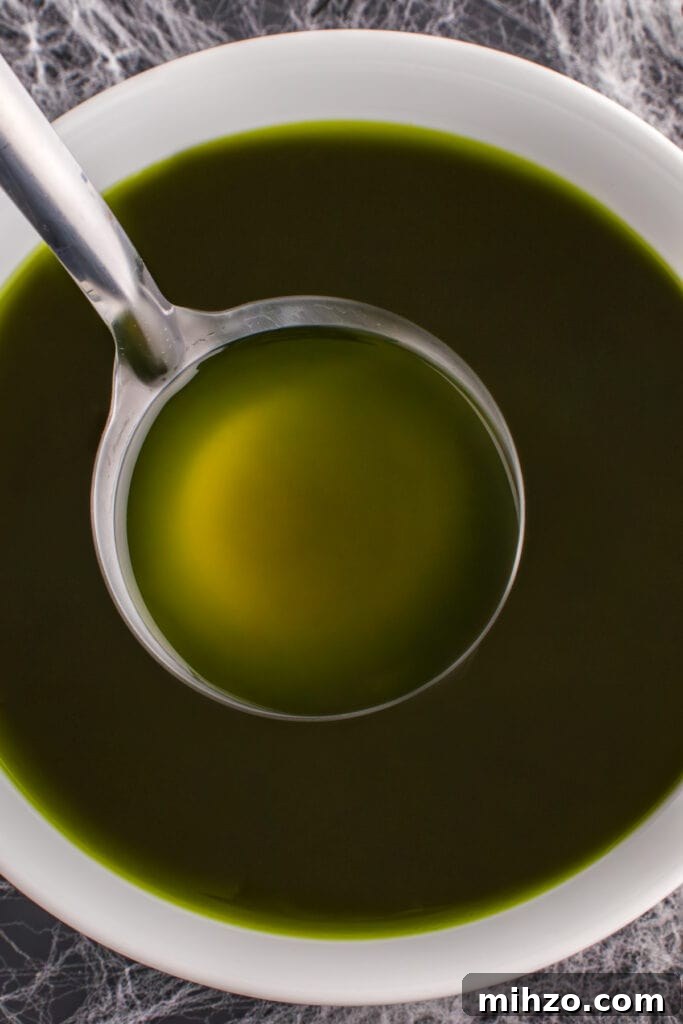 Toxic Waste Punch Recipe: How to Make a Neon Party Drink 13 Ladle dipping into a bowl of dark green Toxic Waste Punch on a Halloween-themed table with cobweb decorations.