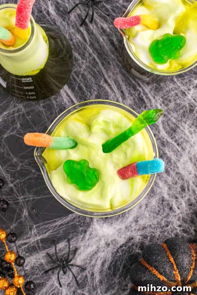 Toxic Waste Punch Recipe: How to Make a Neon Party Drink 16 Beakers of Toxic Waste Punch decorated with gummy worms and gummy frogs on foamy green topping for a creepy Halloween drink.