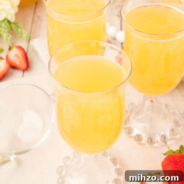 Toxic Waste Punch Recipe: How to Make a Neon Party Drink 19 Square crop showing three glasses of golden mock champagne punch on a light wood table with strawberries scattered nearby.