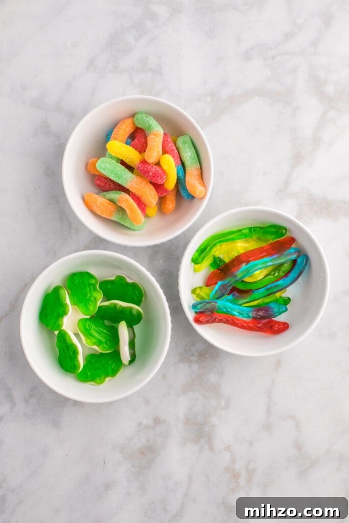 Toxic Waste Punch Recipe: How to Make a Neon Party Drink 5 Three small bowls with gummy candies including sour worms, green gummy frogs, and gummy snakes for punch decoration.