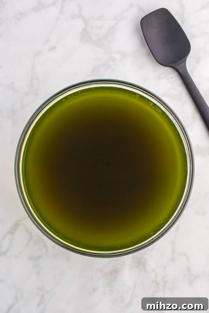 Toxic Waste Punch Recipe: How to Make a Neon Party Drink 7 Large glass bowl of dark green punch after food coloring is added, with a black spatula and green food coloring bottle on the side.