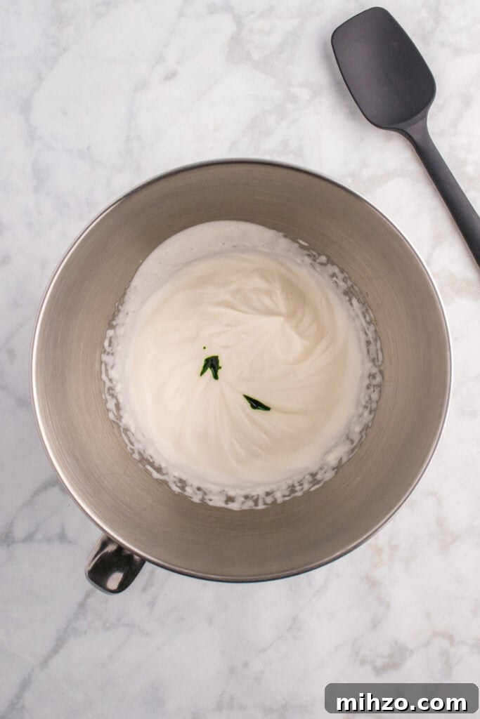 Toxic Waste Punch Recipe: How to Make a Neon Party Drink 10 Mixing bowl with whipped cream partially mixed and drops of green food coloring on top before being swirled.