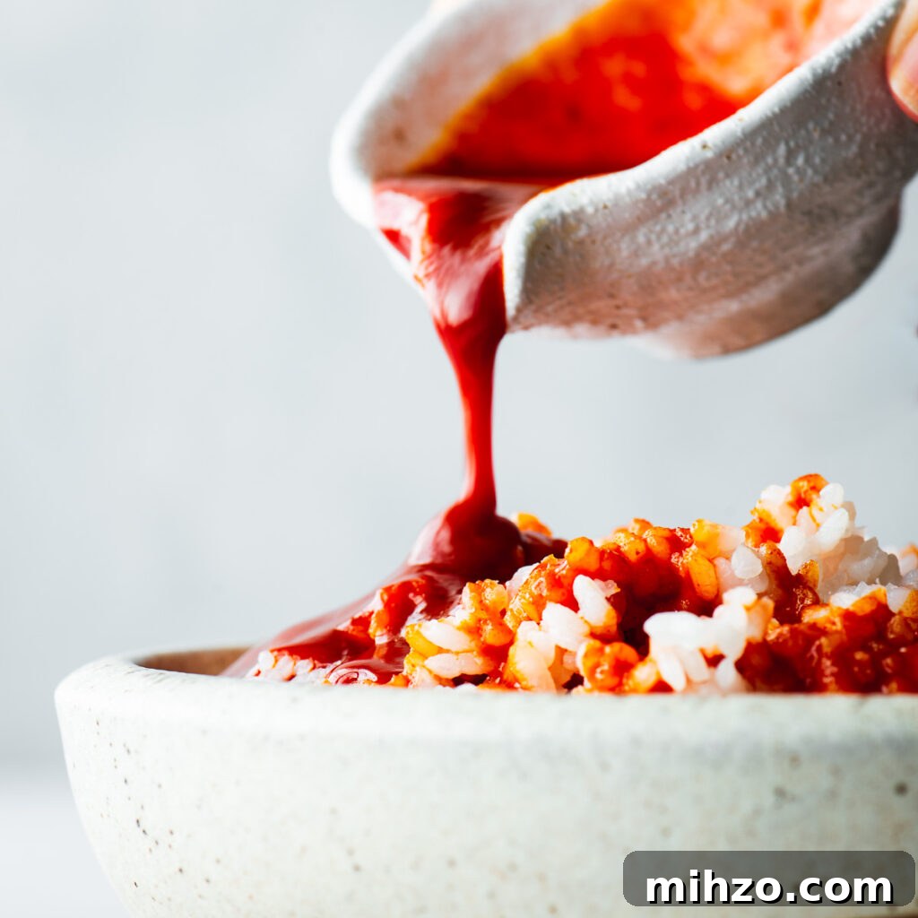 Spicy bibimbap sauce poured over a bowl of steamed white rice.