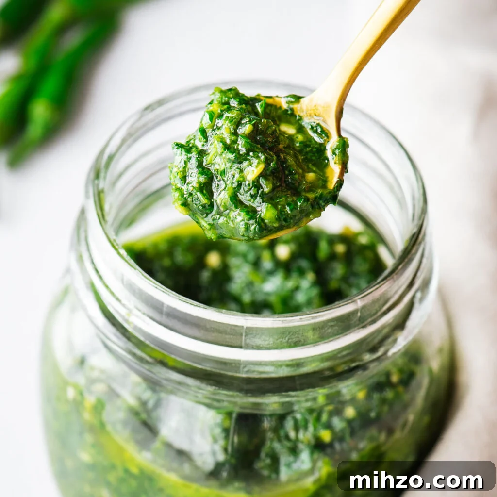A teaspoon of green zhoug sauce being scooped from a glass jar.