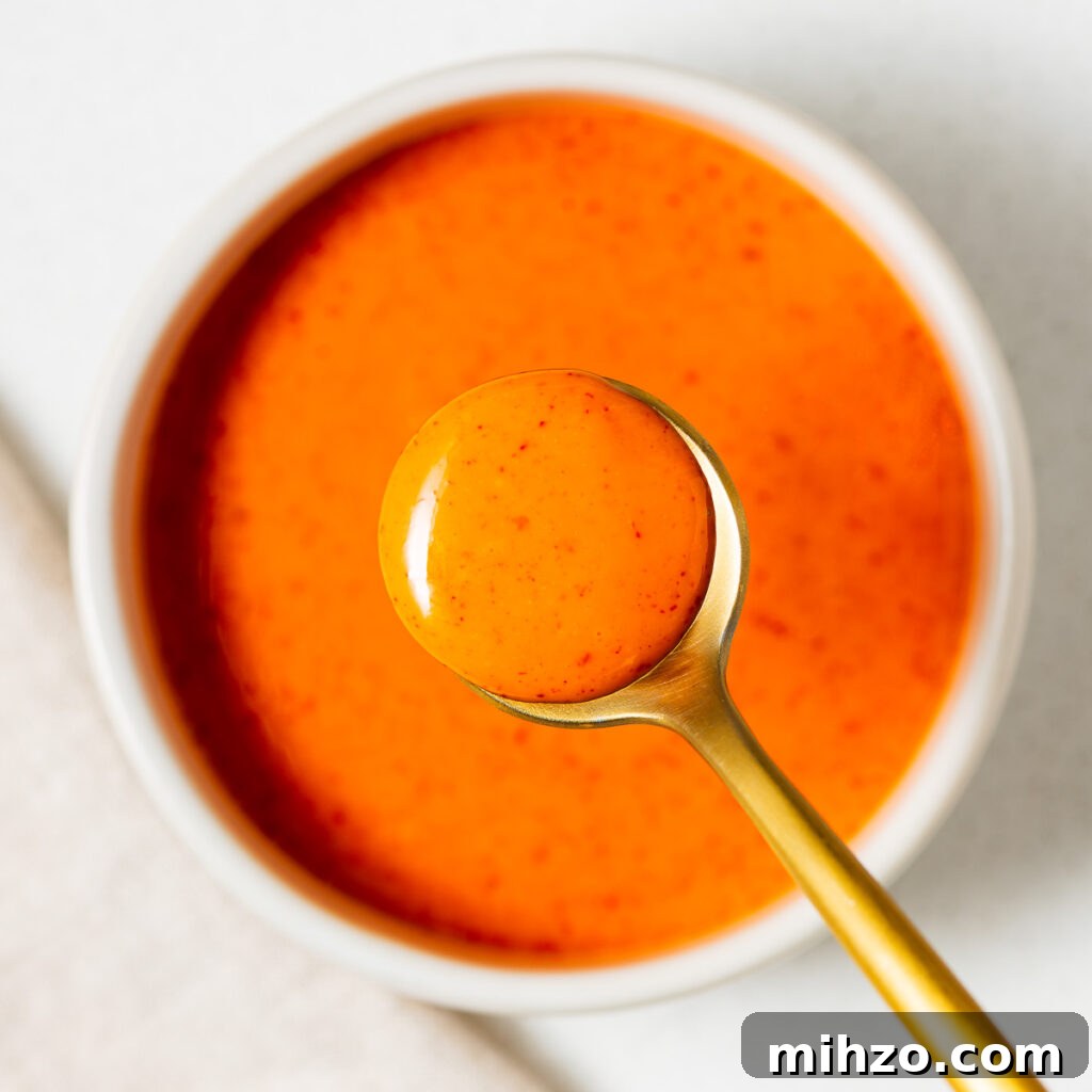 A small white ceramic bowl with bright orange gochujang mayo and a golden serving spoon.