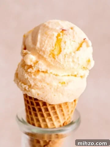 A sugar cone with a scoop of frozen kefir ice cream with fresh peaches.