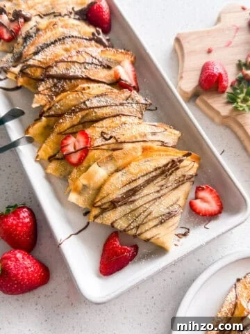 Strawberry Nutella crepes stacked on a plate.