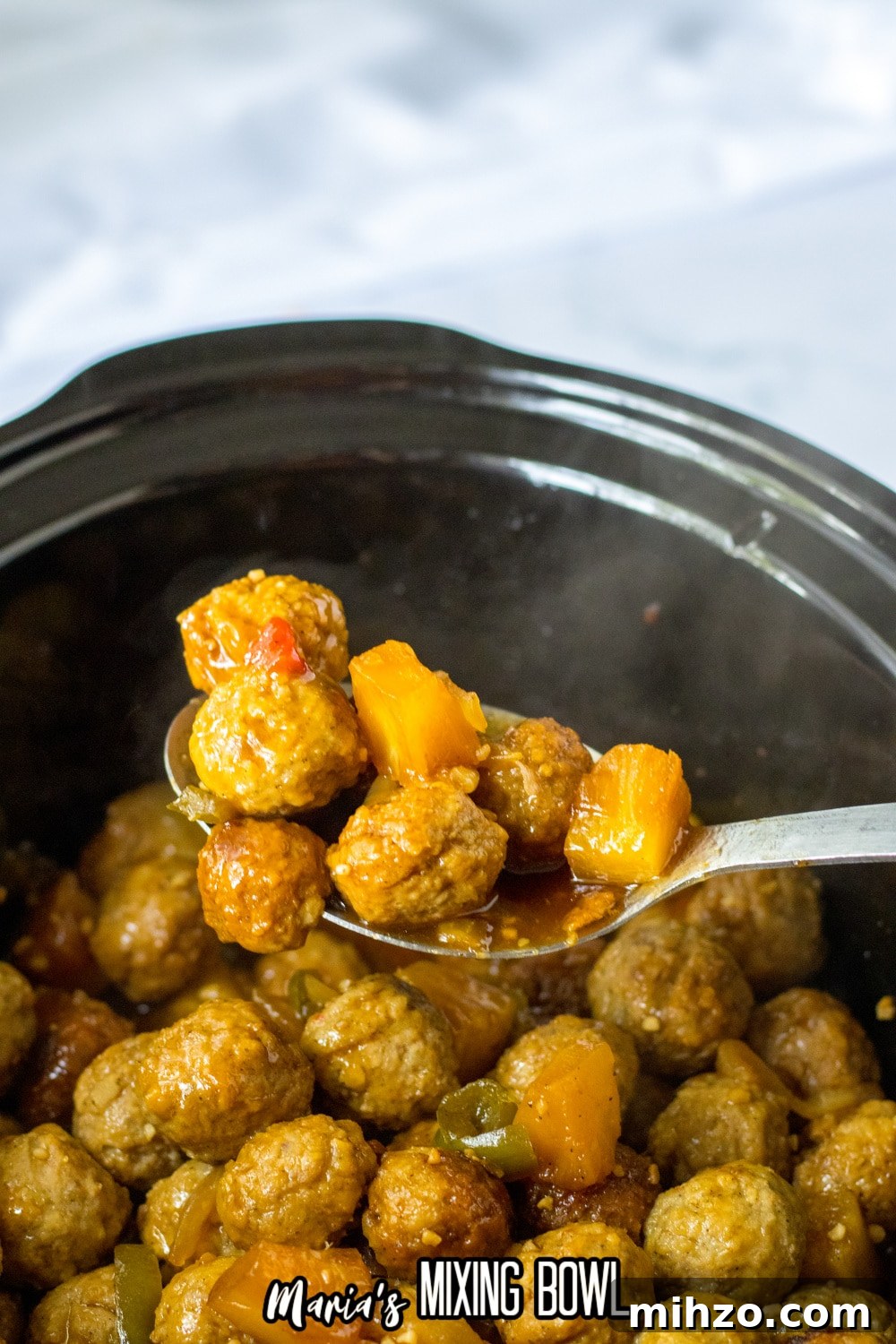 Slow Cooker Hawaiian-Style Pineapple Meatballs 7 large metal spoon full of hawaiian meatballs held above a slow cooker