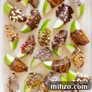 A variety of chocolate dipped apple slices on a cream colored serving platter.