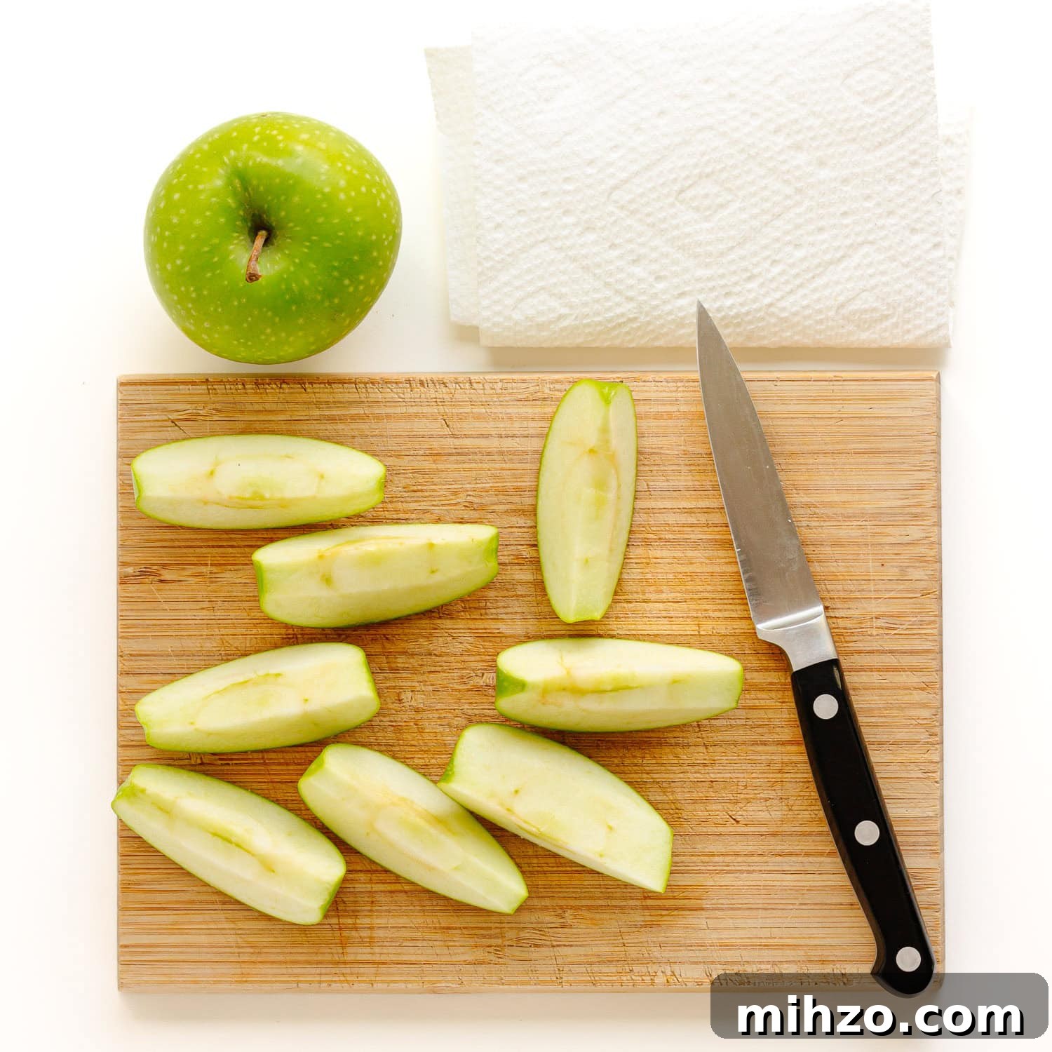 Chocolate-Dipped Apple Slices for Snacks & Parties 5 Apple sliced into wedges on a cutting board with whole apple and paper towel next to it.