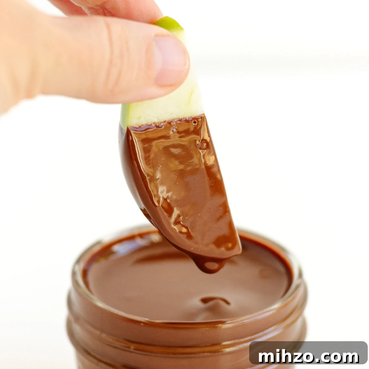 Chocolate-Dipped Apple Slices for Snacks & Parties 7 Hand dipping apple slice into melted chocolate.