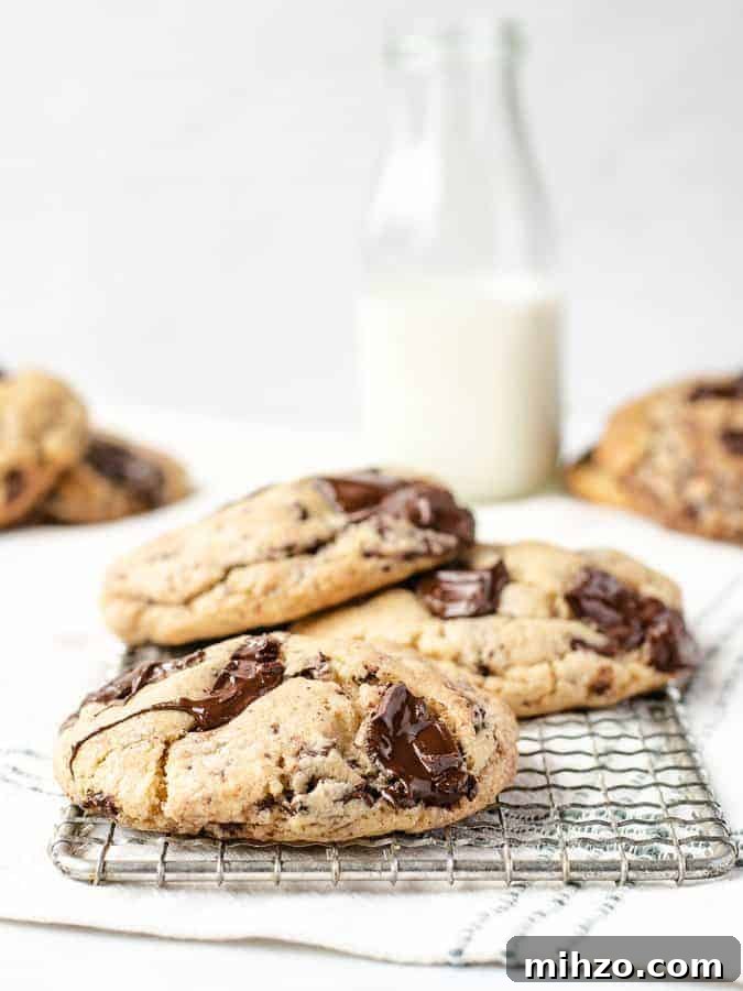 Straight on shot of big soft chocolate chip cookies with melted chocolate on cooling rack with milk behind