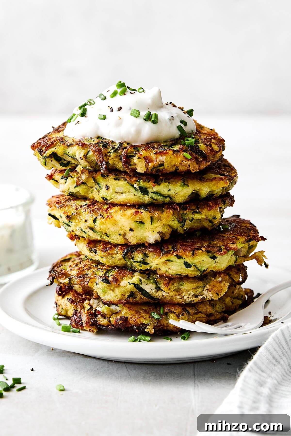Zucchini fritters piled on a plate with yogurt sauce.