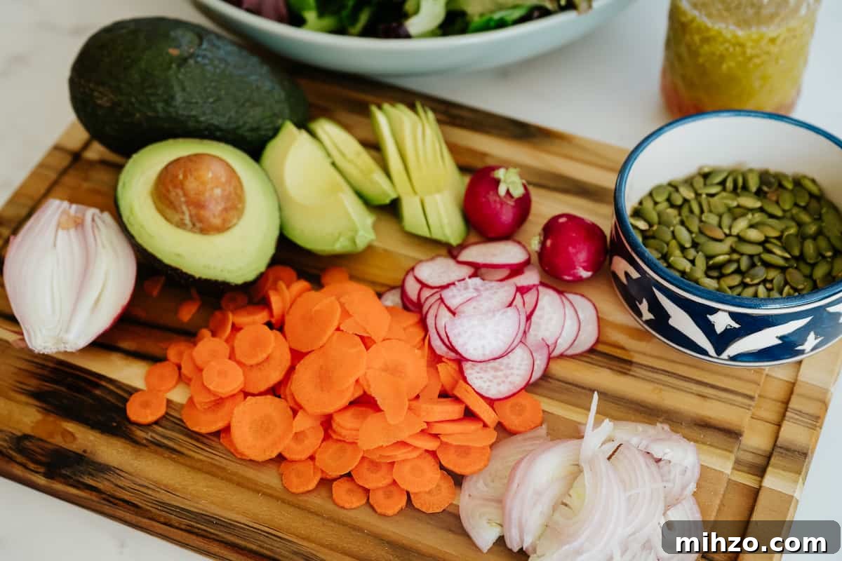 Grilled Carne Asada Steak Salad with Cilantro Lime Dressing 6 add-in ingredients for salad including thinly sliced shallots, radish, carrots, avocado and pepitas on a wooden cutting board.