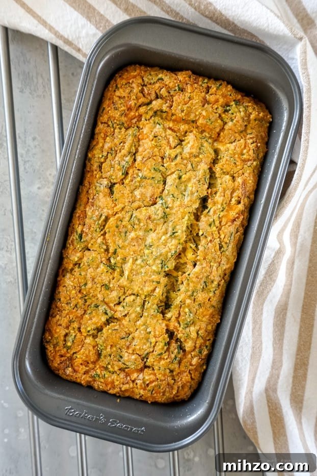 Overhead shot of a cheddar chive zucchini bread in a metal pan, right out of the oven on a metallic grill. 