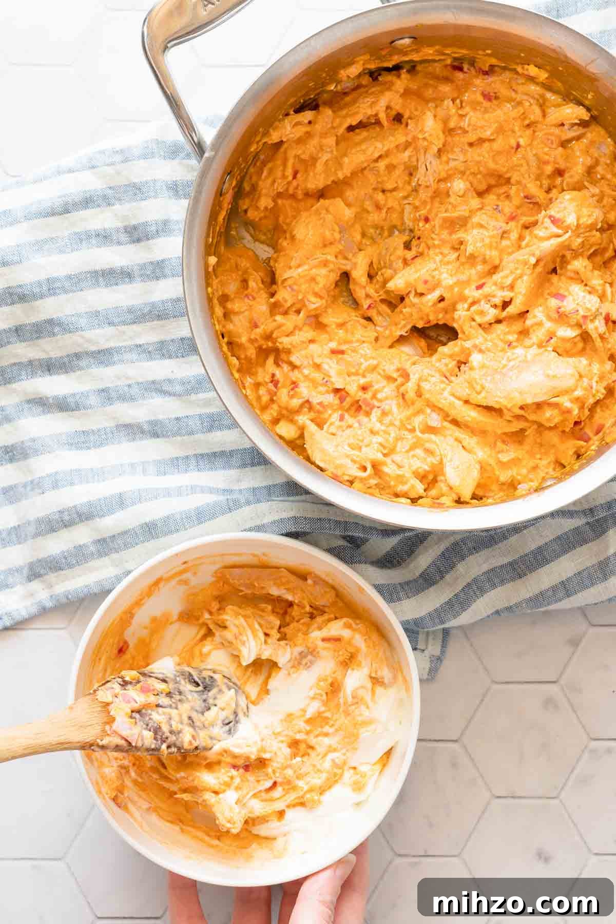 small bowl of yogurt being mixed with some buffalo chicken dip with saucepan of dip on the side.