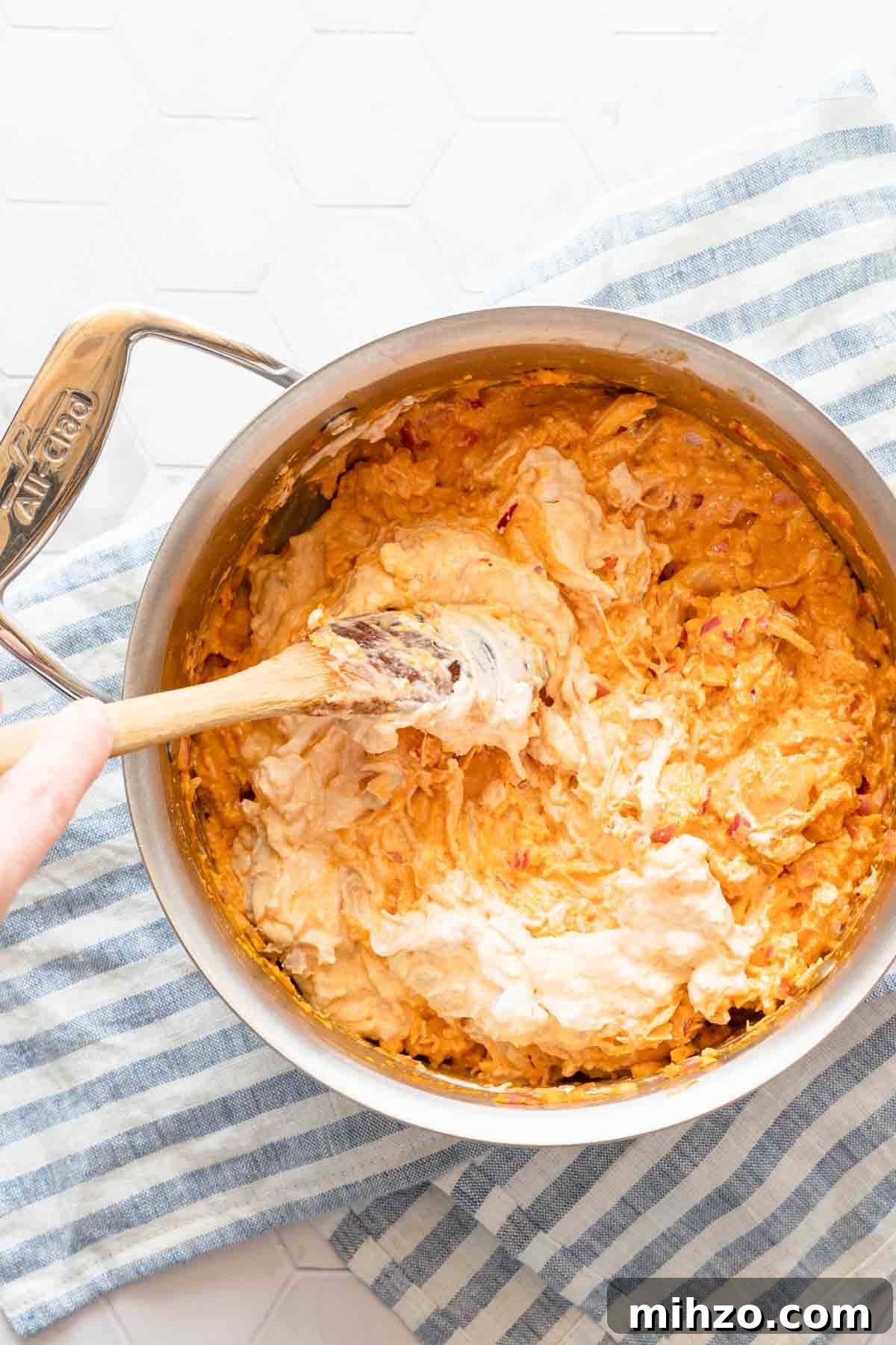 Greek yogurt being stirred into saucepan full of buffalo chicken dip.