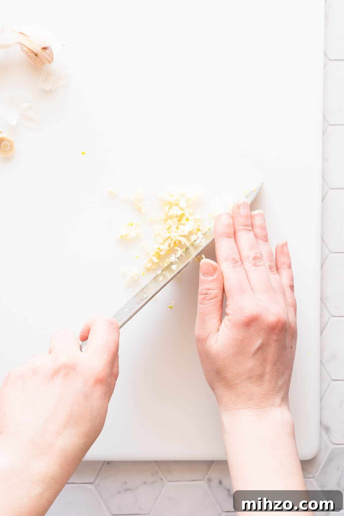 garlic being finely chopped on cutting board.