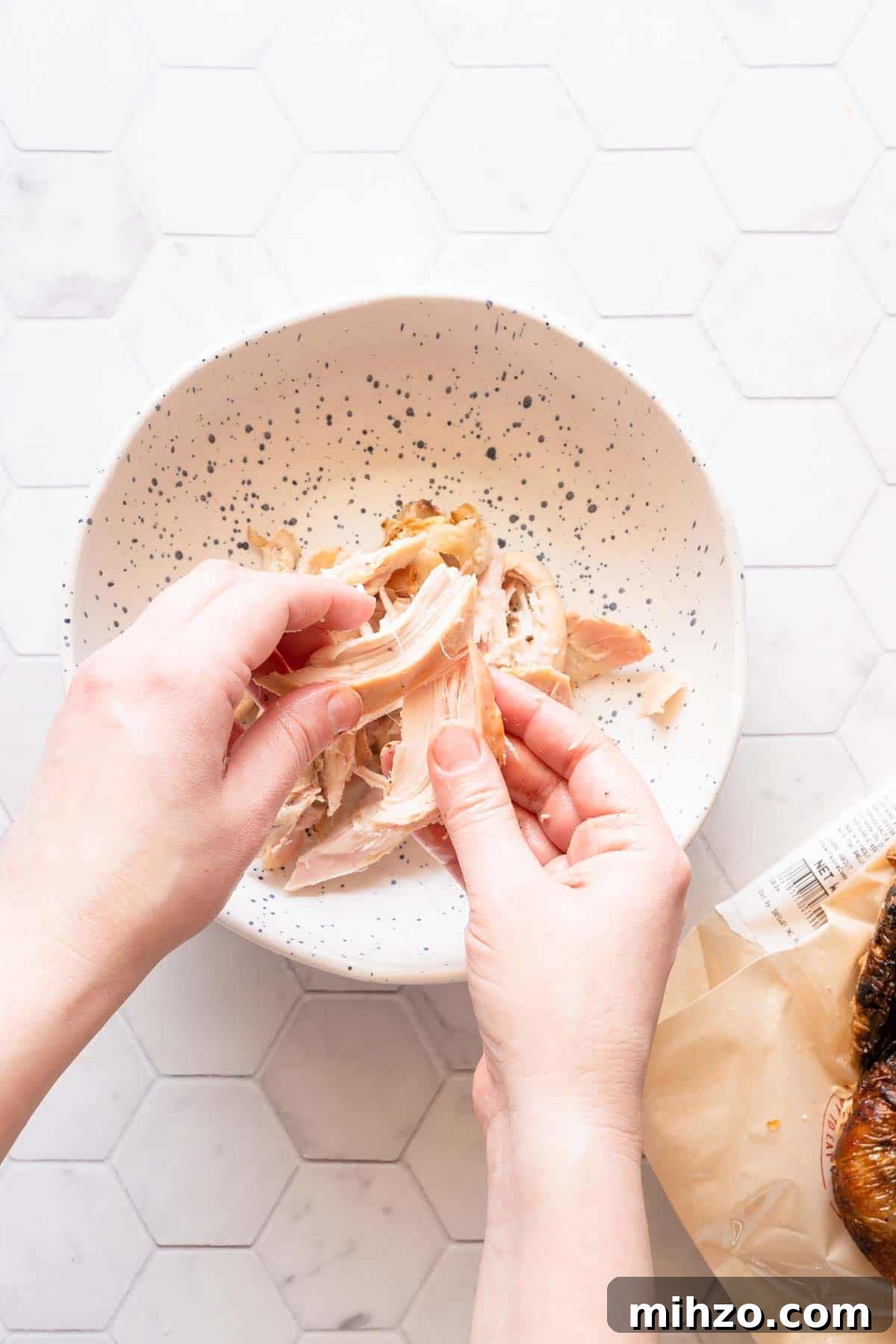 chicken being shredded by hand over a small bowl.