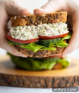 Tuna Salad Sandwich holding sandwich close to camera with second sandwich blurred in background on wooden board