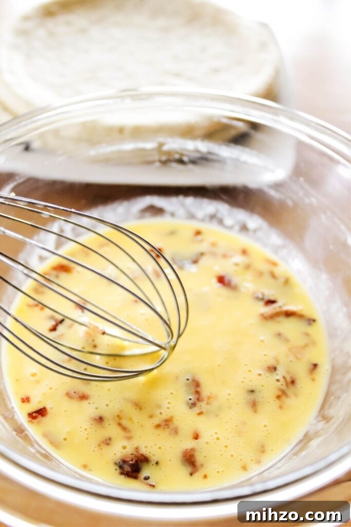 eggs whisked in a bowl with bacon and pizza crust on counter behind it 