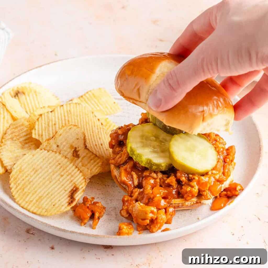 Ground Chicken Sloppy Joes with Tangy BBQ Sauce 7 hand adding bun top to sloppy Joe sandwich with chips on the side.