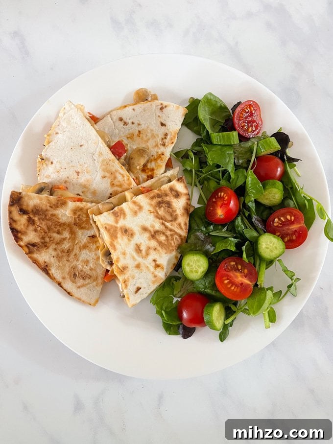 Cheesy Veggie Quesadillas with Roasted Peppers and Spinach 2 Cheesy veggie quesadillas served on a white plate alongside a small salad.