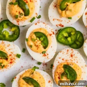 Spicy Deviled Eggs with Sriracha and Smoked Paprika 11 Deviled eggs on white serving dish topped with chopped chives, jalapeño, and paprika.