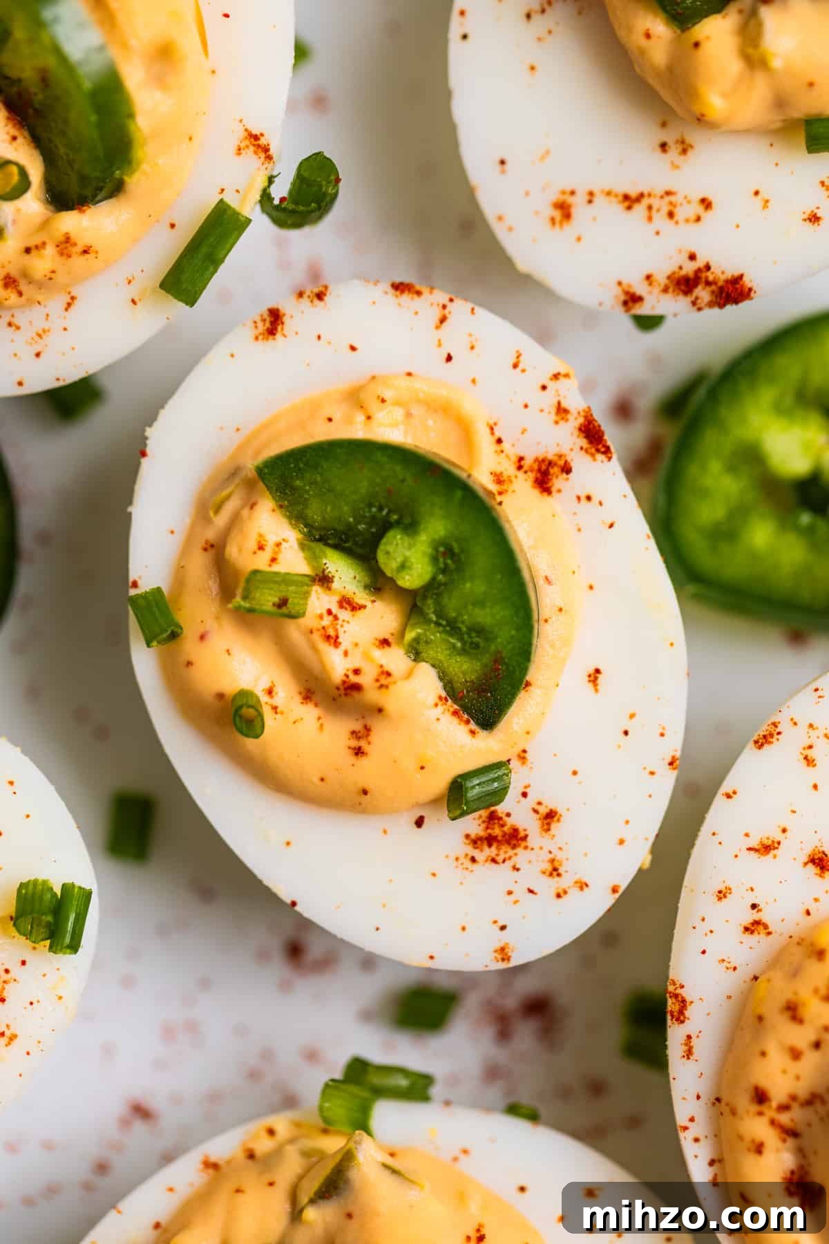 Spicy Deviled Eggs with Sriracha and Smoked Paprika 3 Close up view of spicy deviled egg on plate with slice of jalapeño and paprika on top.