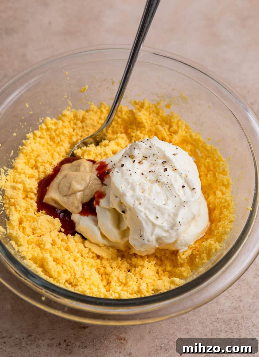 Spicy Deviled Eggs with Sriracha and Smoked Paprika 6 Mashed egg yolk, mayonnaise, dijon mustard and other ingredients in glass bowl with spoon.